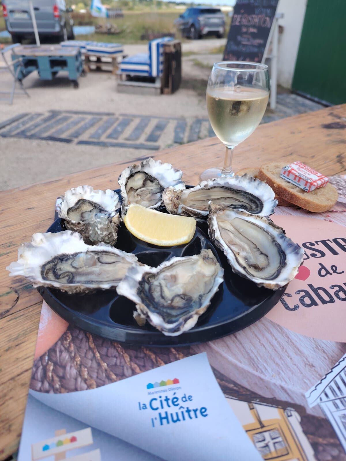 Un plateau d'huîtres ouvertes, citron, pain beurré et verre de vin blanc en terrasse