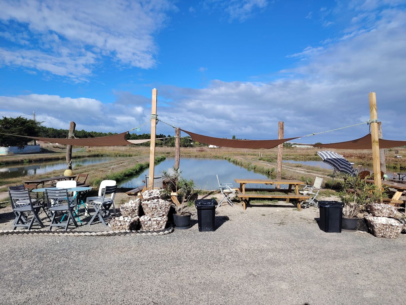 Vue d'ensemble de la terrasse, ses tables et ses voiles face aux claires